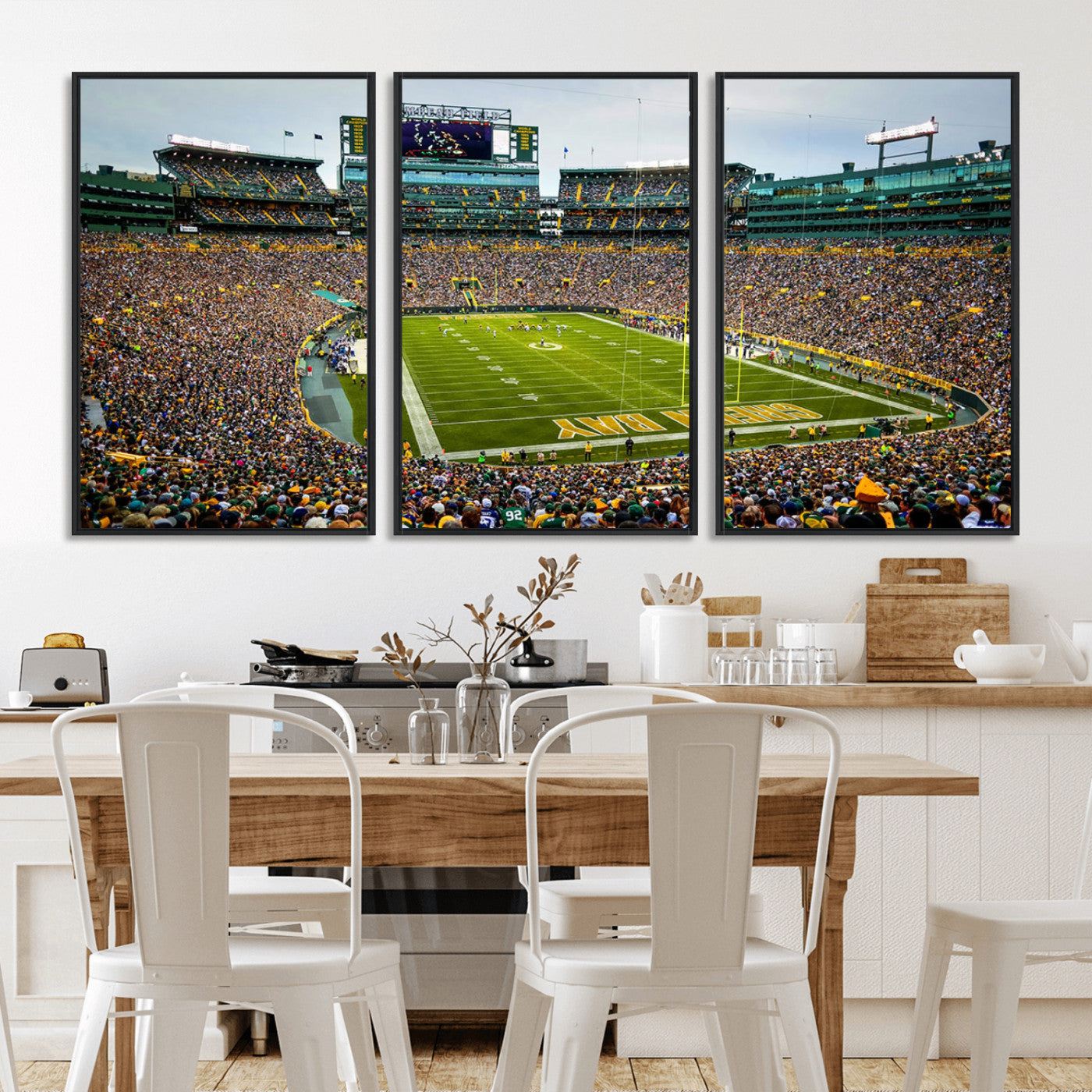 Packed football stadium with thousands of fans watching an American football game on a well-maintained field. The scoreboard displays "Lambeau Field," and players are lined up on the field. The stadium is surrounded by multiple tiers of seating filled wit