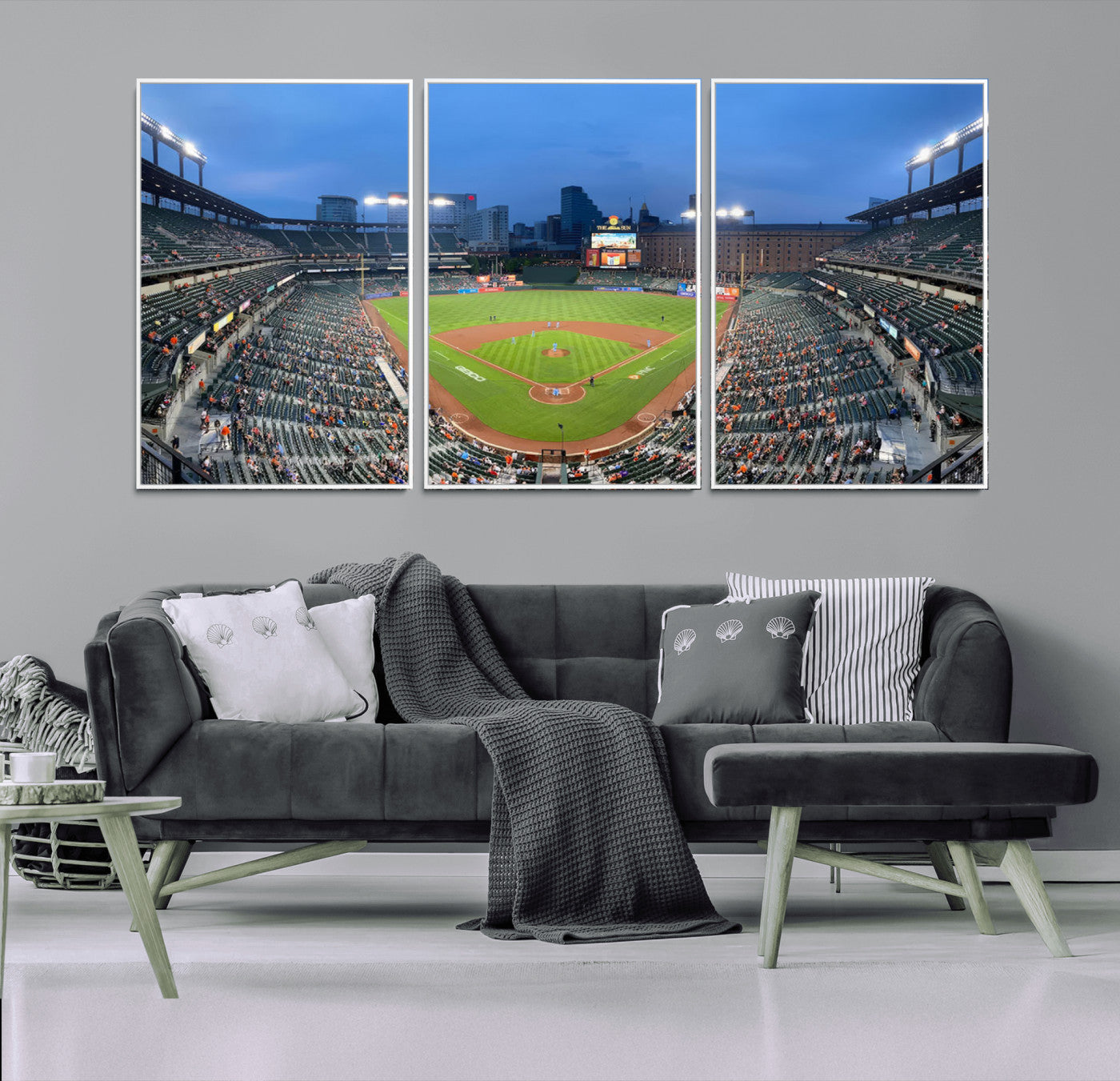 Wide panoramic view of a baseball stadium at dusk with players on the field, stadium lights illuminating the scene, and a sparse crowd of spectators in the stands.