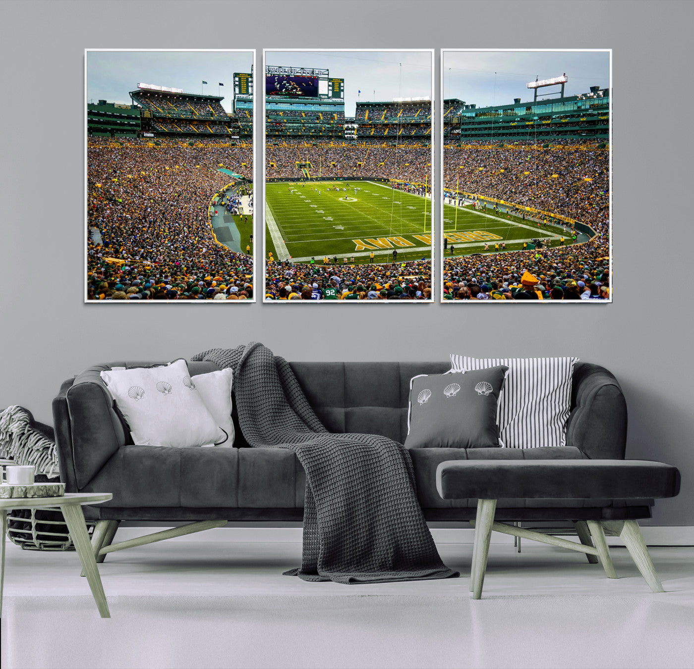 Packed football stadium with thousands of fans watching an American football game on a well-maintained field. The scoreboard displays "Lambeau Field," and players are lined up on the field. The stadium is surrounded by multiple tiers of seating filled wit