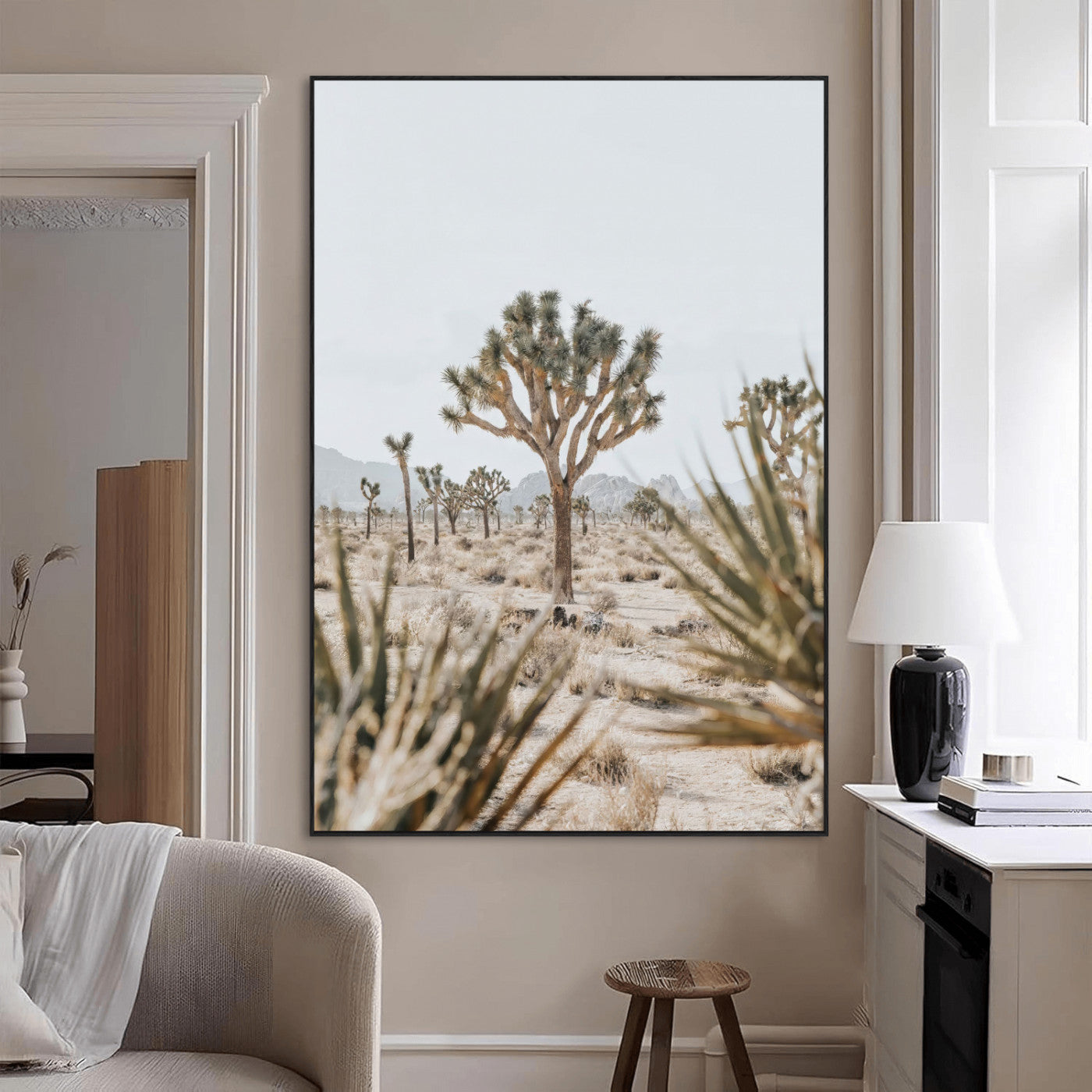 A wide desert landscape featuring multiple Joshua trees with spiky leaves and twisted branches, set against a pale sky and distant rocky hills. The foreground has blurred desert shrubs, emphasizing depth.