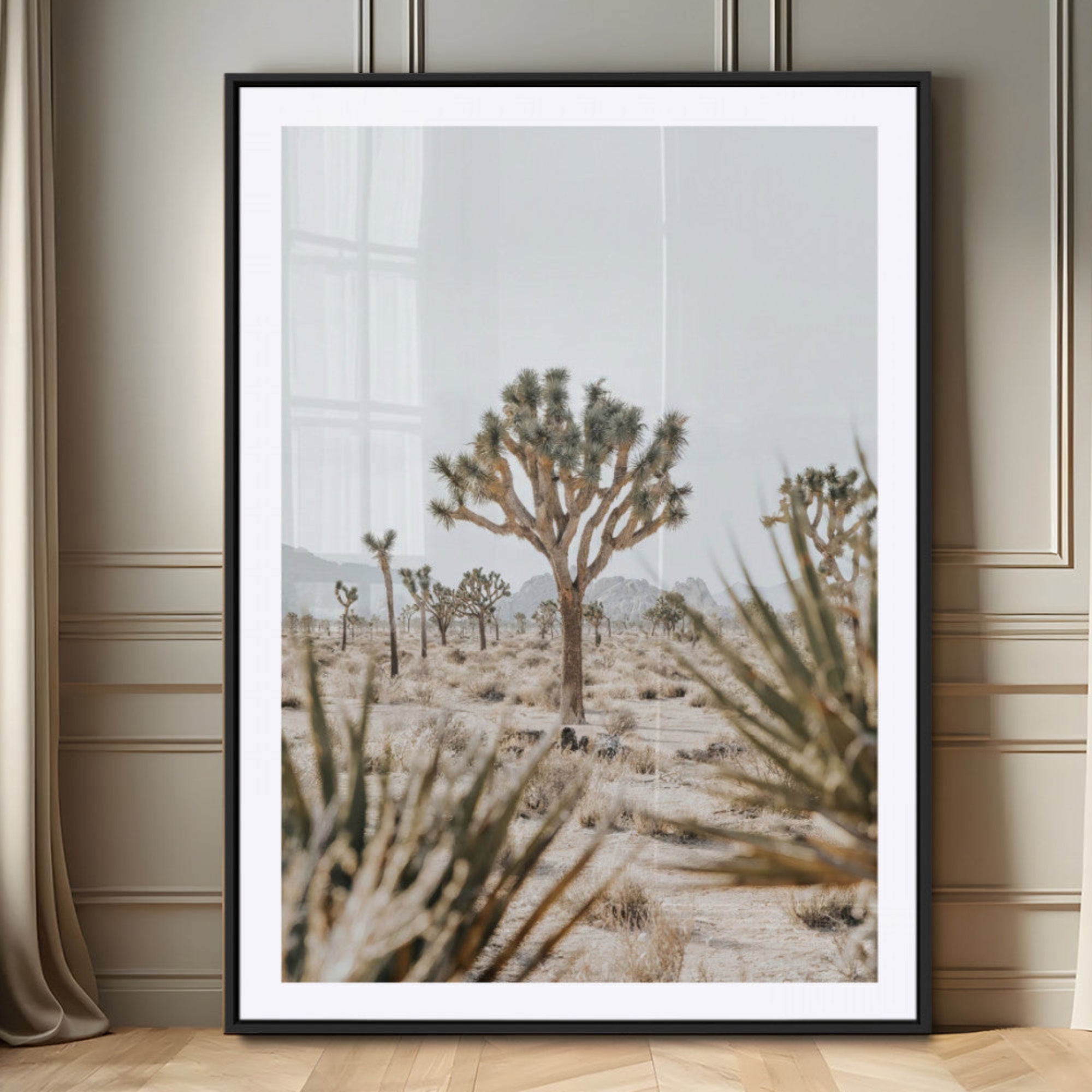 A wide desert landscape featuring multiple Joshua trees with spiky leaves and twisted branches, set against a pale sky and distant rocky hills. The foreground has blurred desert shrubs, emphasizing depth.