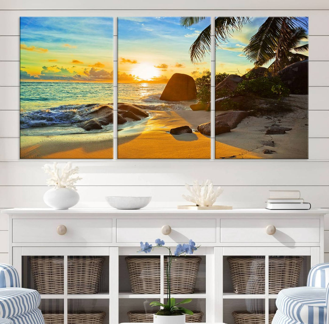 The Serene Tropical Beach Sunset Canvas Wall Art, a 3-panel giclee print, beautifully captures an ocean sunset with its depiction of palm trees and a coastal rock formation.