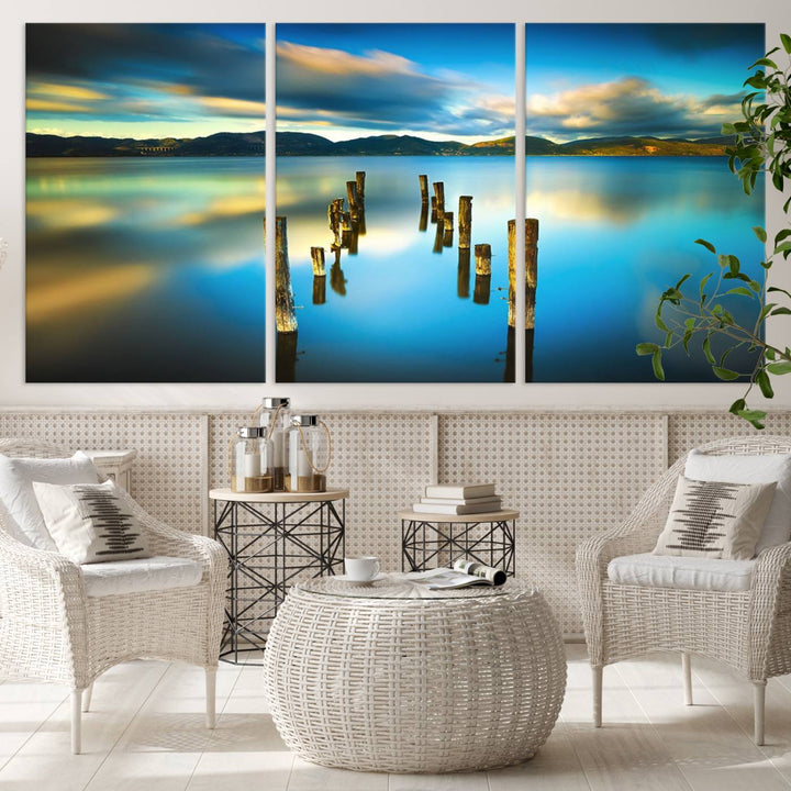 A triptych of a serene lake scene with old wooden pillars, blue sky, and clouds casts a coastal ambiance. The Sea Ocean Sunset Beach Wall Art Canvas Print reflects the soothing nature of the ocean.