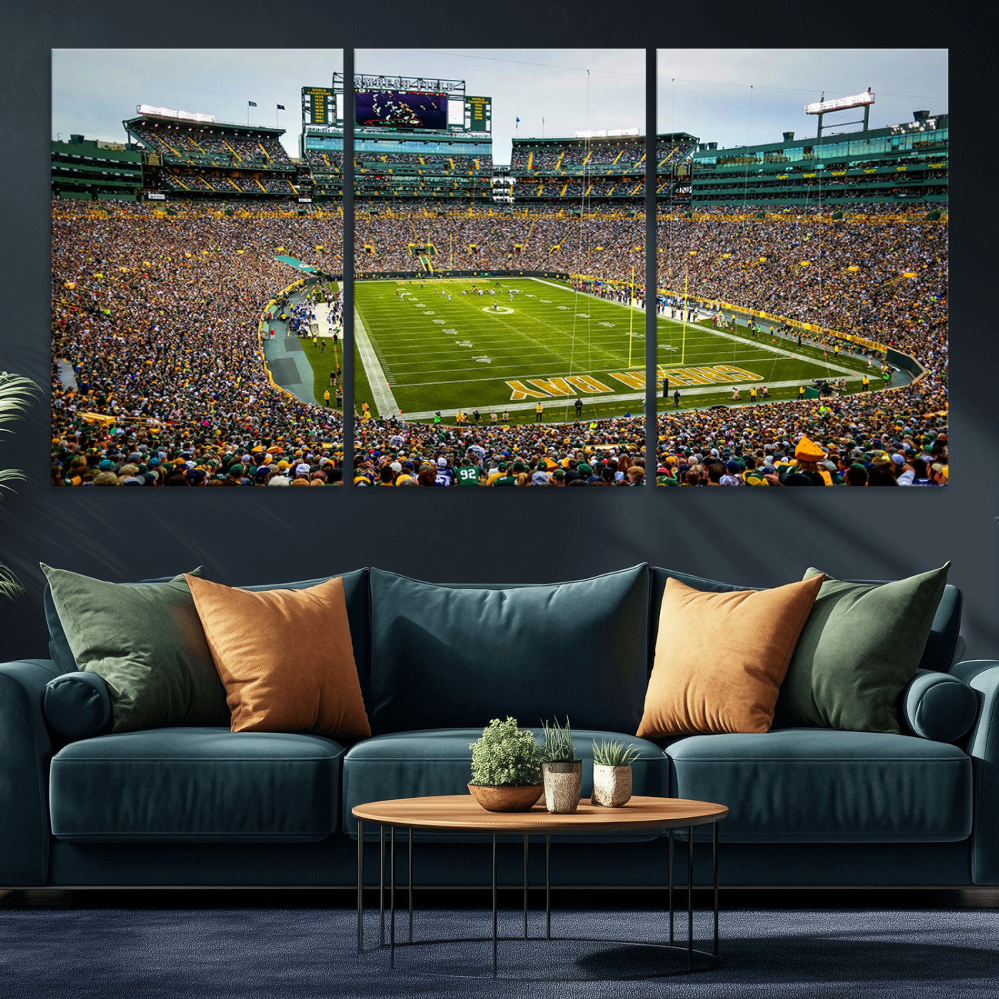 Packed football stadium with thousands of fans watching an American football game on a well-maintained field. The scoreboard displays "Lambeau Field," and players are lined up on the field. The stadium is surrounded by multiple tiers of seating filled wit