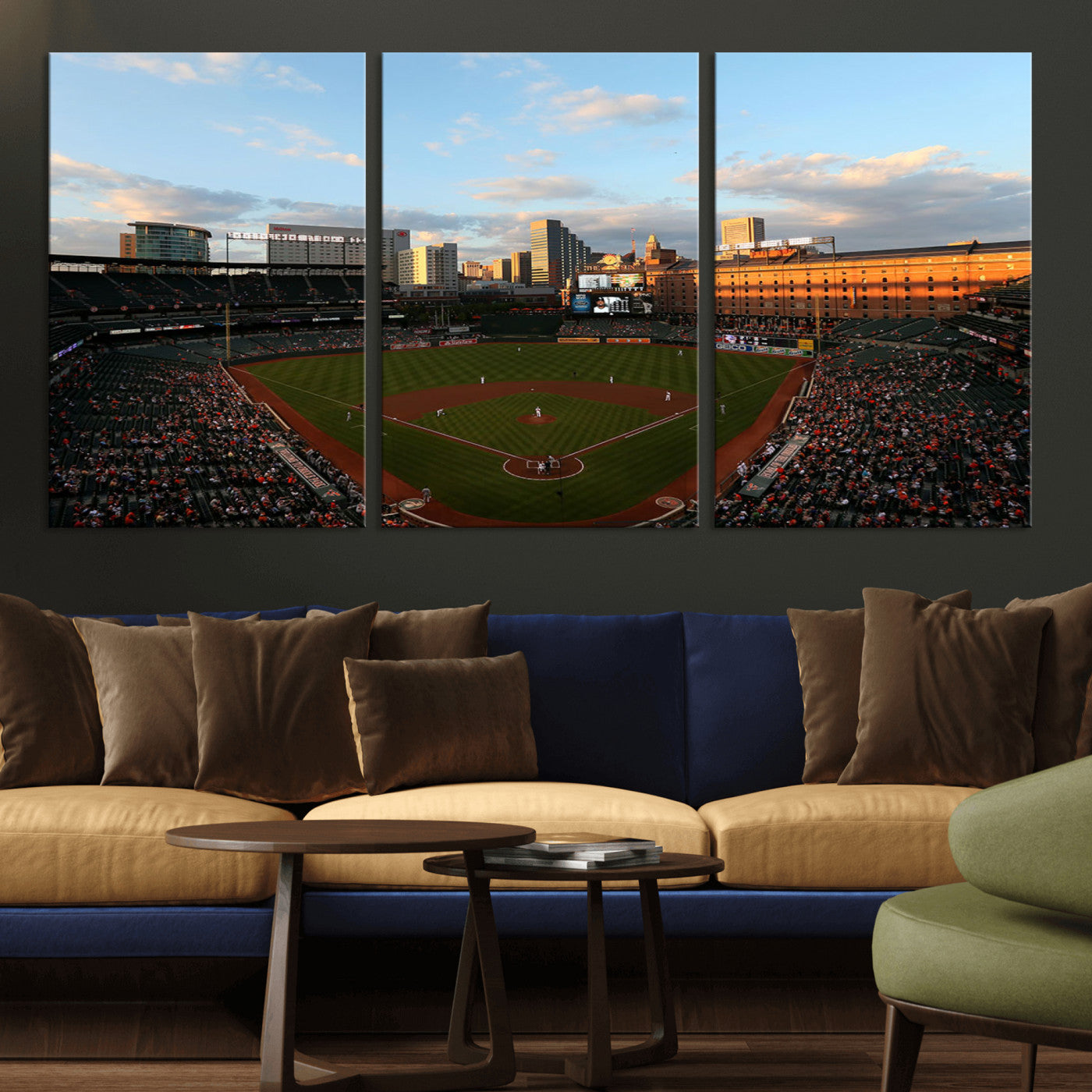 Aerial view of a baseball stadium at sunset with players on the field, fans in the stands, a city skyline in the background, and the setting sun casting warm light on the buildings.