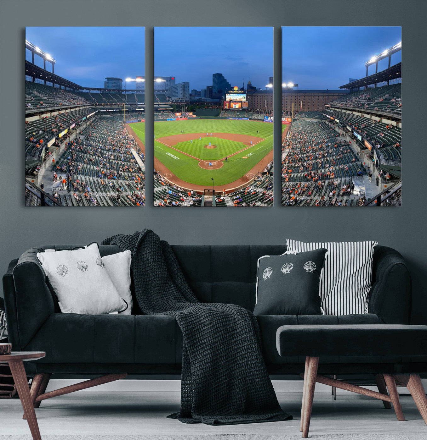 Wide panoramic view of a baseball stadium at dusk with players on the field, stadium lights illuminating the scene, and a sparse crowd of spectators in the stands.