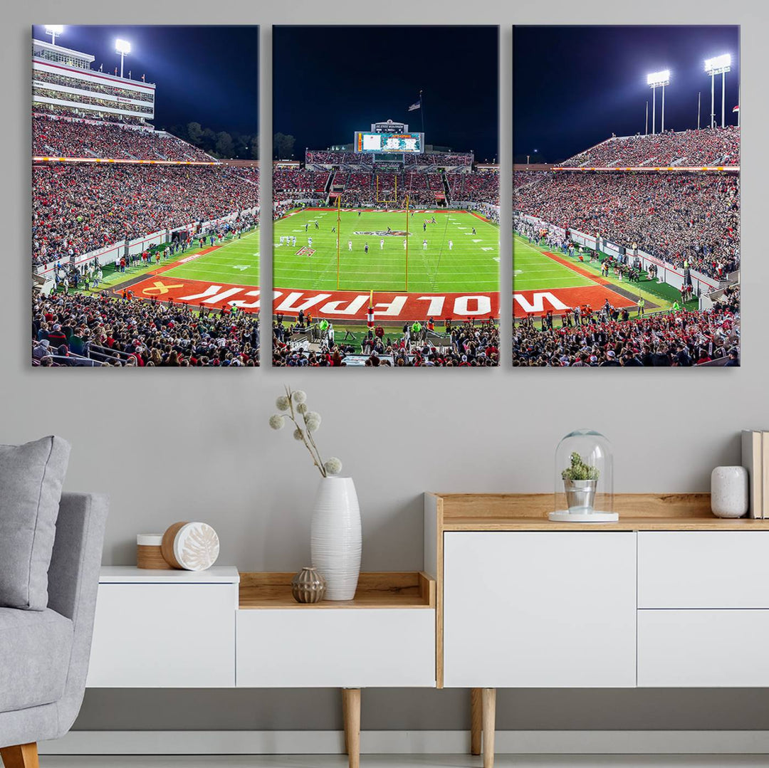 A NC State Wolfpack Football Team print of Carter-Finley Stadium at night features WOLFPACK illuminated brightly in the end zone grass.