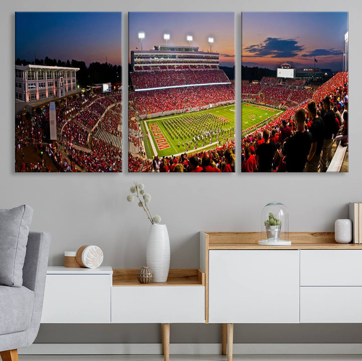 A print of a bustling Carter-Finley Stadium at dusk, featuring fans and a band, captures the essence of NC State Wolfpack football.