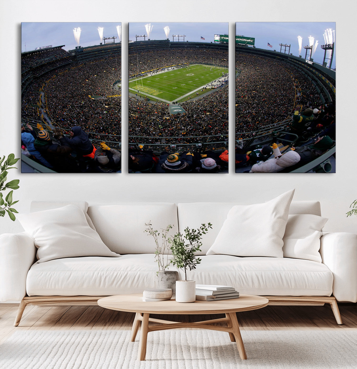 Wide fisheye view of a packed Lambeau Field stadium during an American football game. The crowd fills the stands, and fireworks are going off above the stadium lights. The scoreboard displays "Touchdown," and the field has "Packers" painted in the end zon