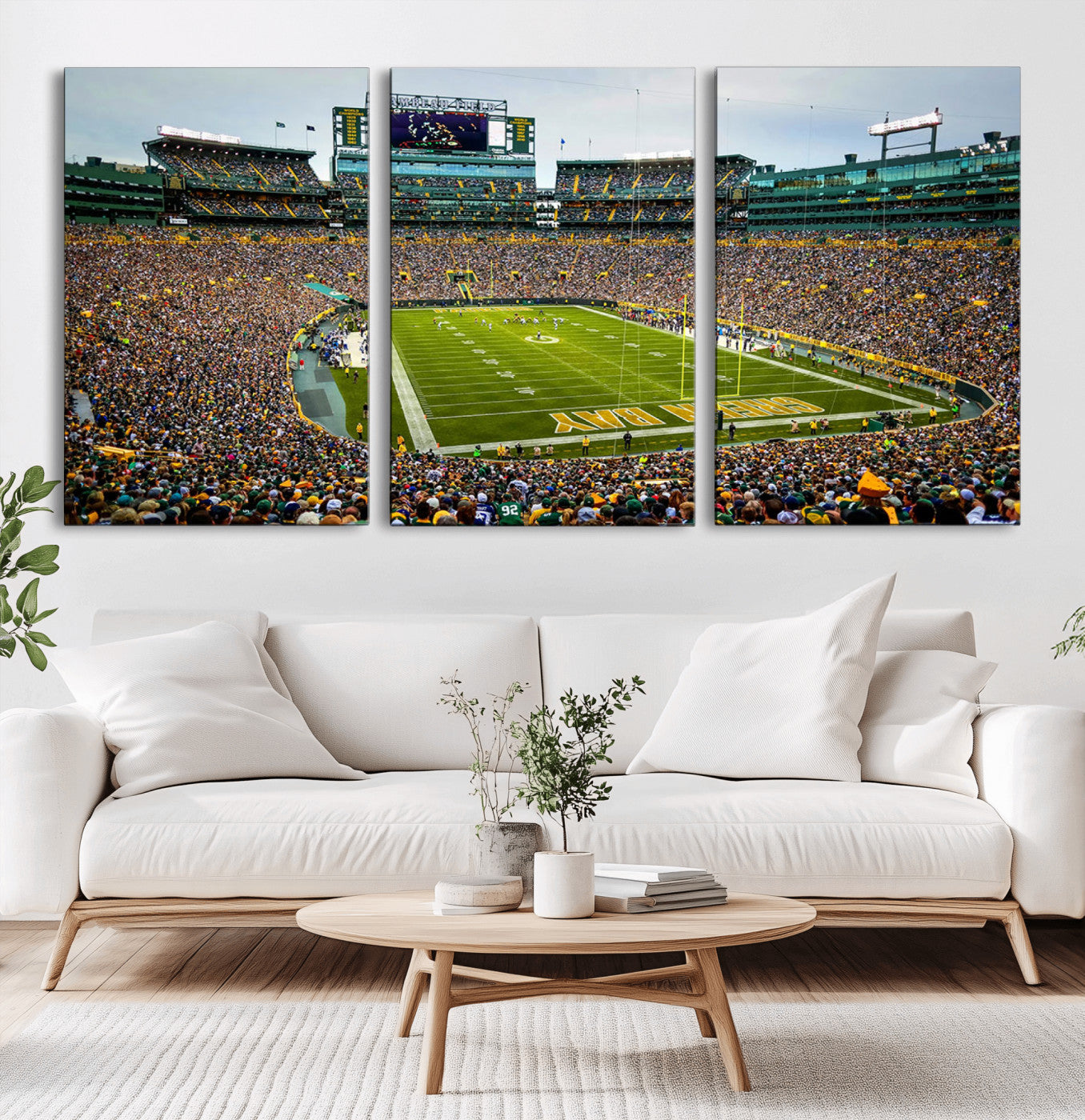 Packed football stadium with thousands of fans watching an American football game on a well-maintained field. The scoreboard displays "Lambeau Field," and players are lined up on the field. The stadium is surrounded by multiple tiers of seating filled wit