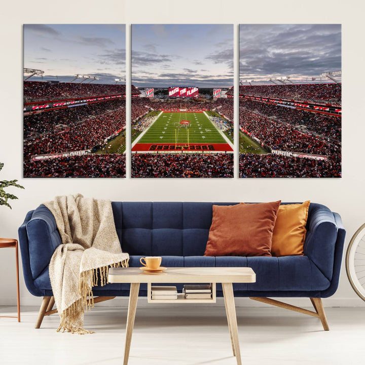 The wall art captures a stunning scene of Raymond James Stadium bathed in the warm hues of sunset. The sky, filled with clouds, provides a dramatic contrast to the vibrant lighting on the field, encapsulating the dynamic energy of a football game.