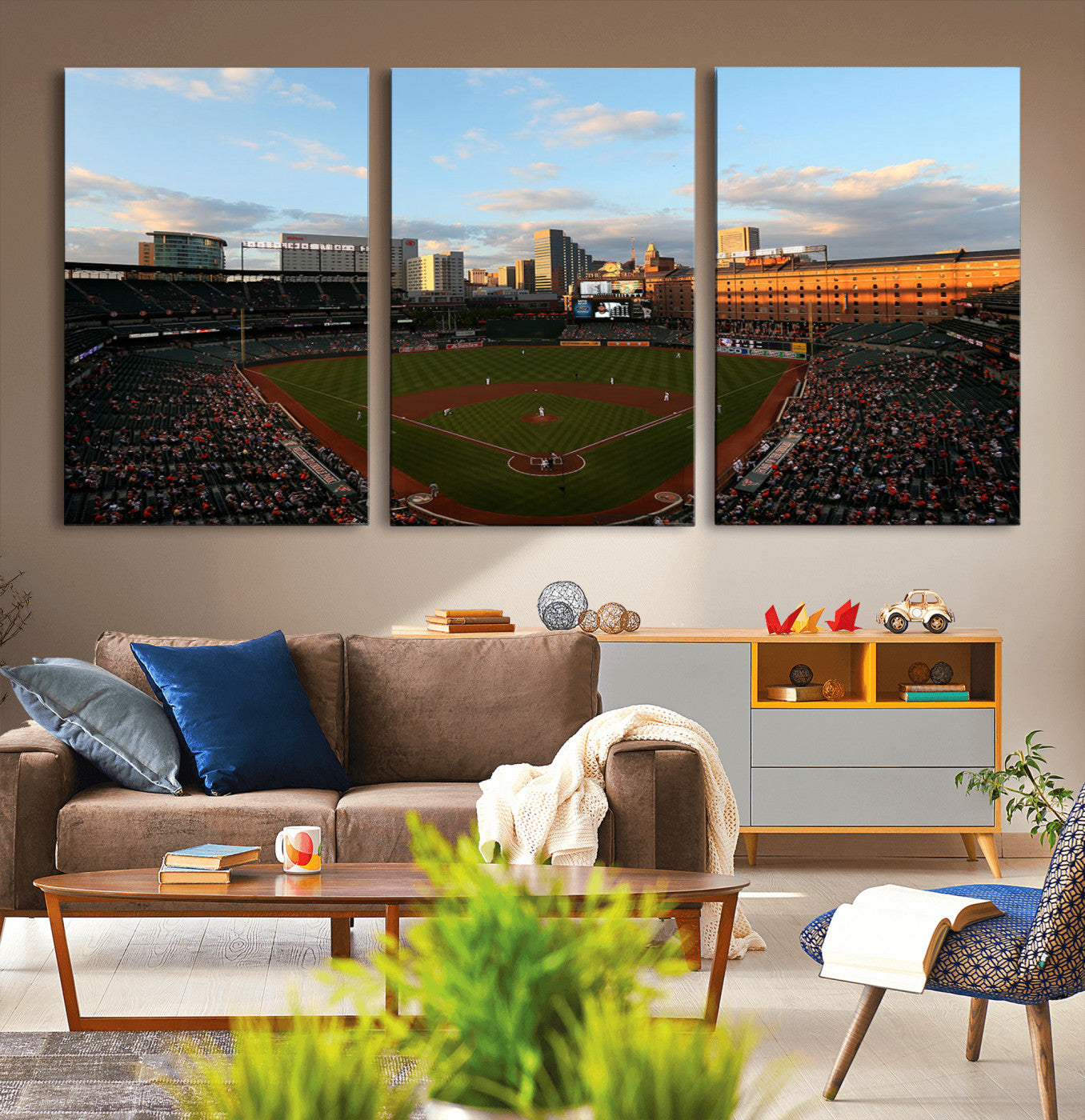 Aerial view of a baseball stadium at sunset with players on the field, fans in the stands, a city skyline in the background, and the setting sun casting warm light on the buildings.