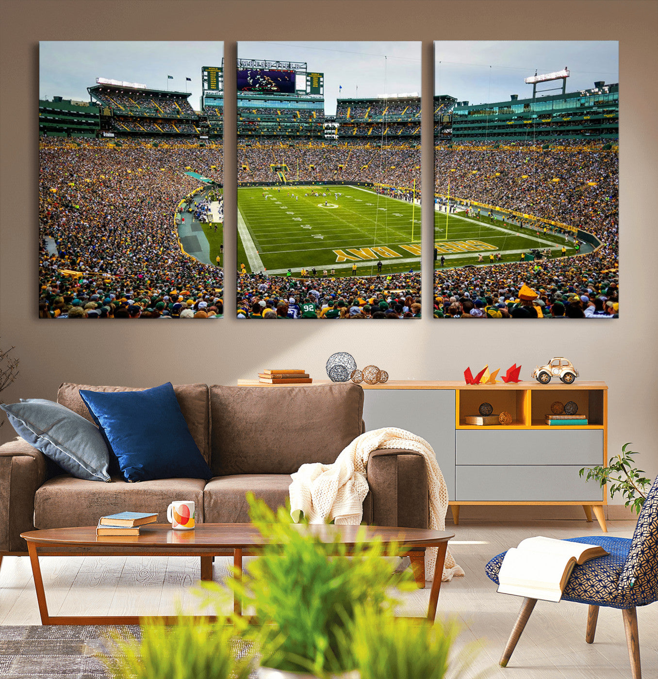 Packed football stadium with thousands of fans watching an American football game on a well-maintained field. The scoreboard displays "Lambeau Field," and players are lined up on the field. The stadium is surrounded by multiple tiers of seating filled wit
