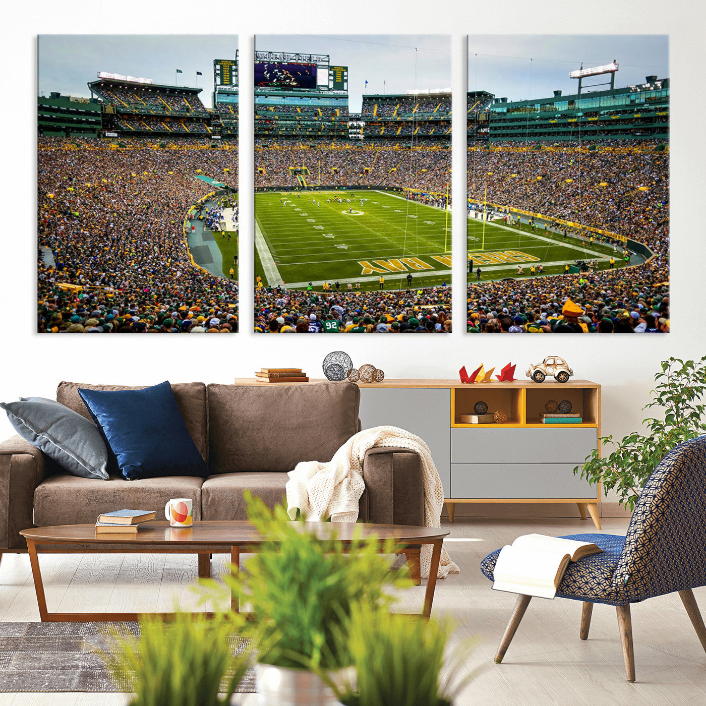 Packed football stadium with thousands of fans watching an American football game on a well-maintained field. The scoreboard displays "Lambeau Field," and players are lined up on the field. The stadium is surrounded by multiple tiers of seating filled wit