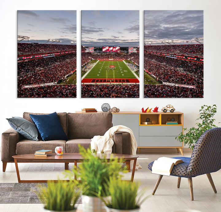 The wall art captures a stunning scene of Raymond James Stadium bathed in the warm hues of sunset. The sky, filled with clouds, provides a dramatic contrast to the vibrant lighting on the field, encapsulating the dynamic energy of a football game.