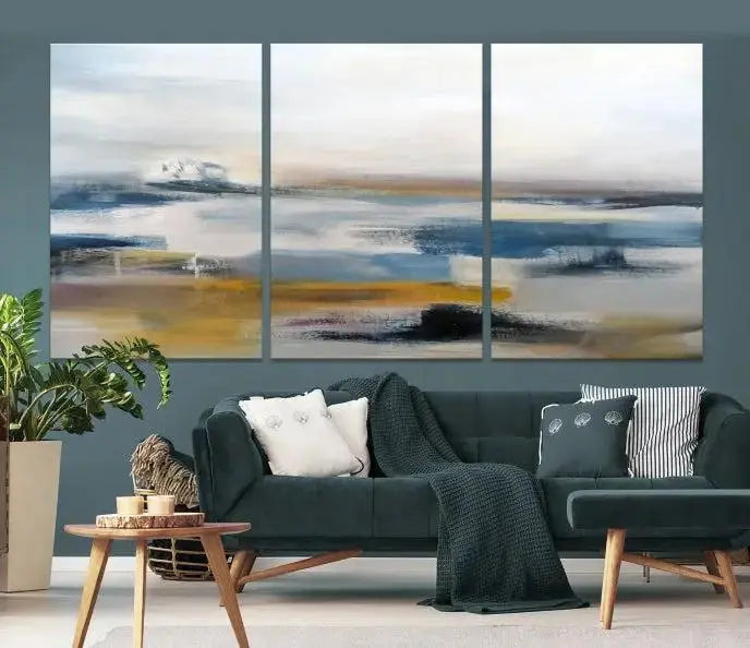 The Abstract Landscape Wall Art Canvas, featuring a 3-panel design in blue, gold, and white, seamlessly blends into the chic modern decor of the living room. This large abstract print enhances the space with its elegant presence.