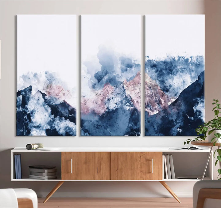 The modern living room features a framed triptych art on a dark wall, complemented by the Abstract Watercolor Mountain Landscape Art Canvas Print, which adds elegance and depth to the space.