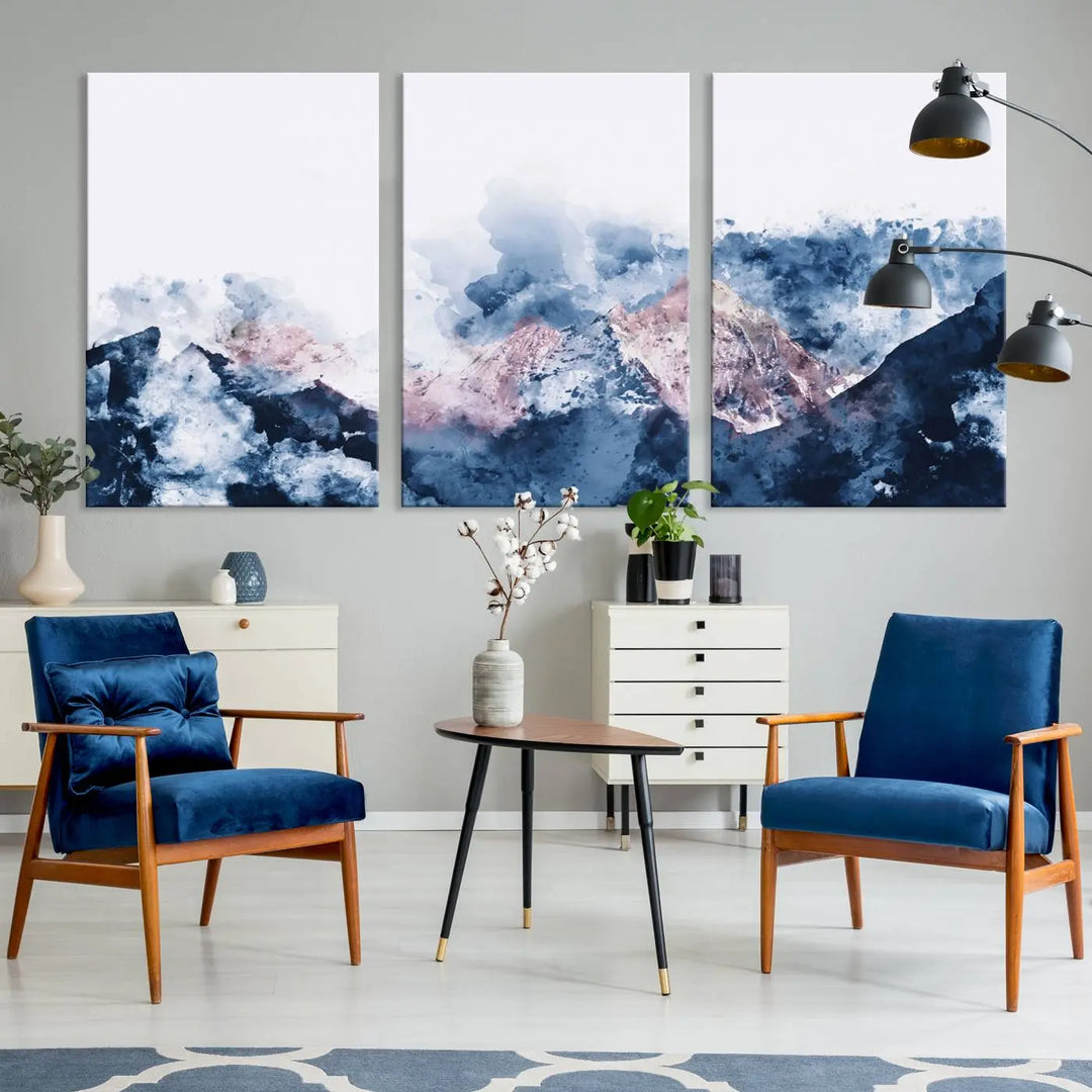 The modern living room features a framed triptych art on a dark wall, complemented by the Abstract Watercolor Mountain Landscape Art Canvas Print, which adds elegance and depth to the space.