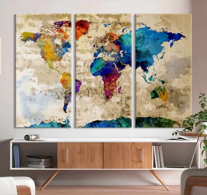 A three-panel "Watercolor Wall Art World Map w/ Antarctica Canvas Print" on museum-quality canvas features vibrant colors and is ready to hang in a dimly lit living room.