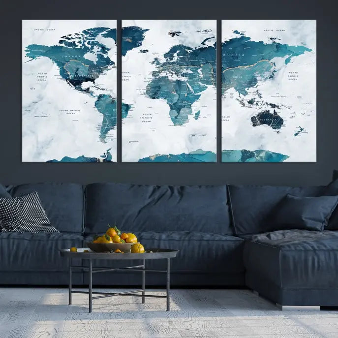 A Push Pin World Map with Antarctica, printed on museum-quality canvas portraying blue oceans, is displayed as a triptych above a dark wall.