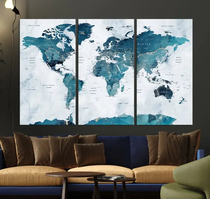 A Push Pin World Map with Antarctica, printed on museum-quality canvas portraying blue oceans, is displayed as a triptych above a dark wall.