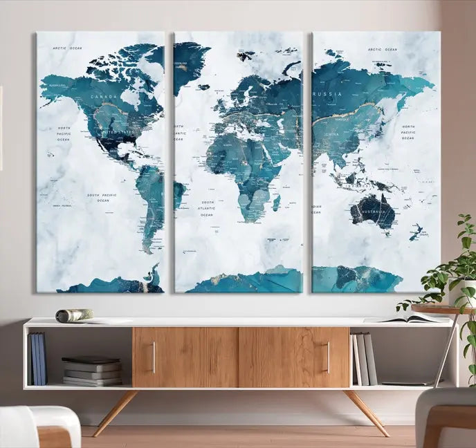 A Push Pin World Map with Antarctica, printed on museum-quality canvas portraying blue oceans, is displayed as a triptych above a dark wall.