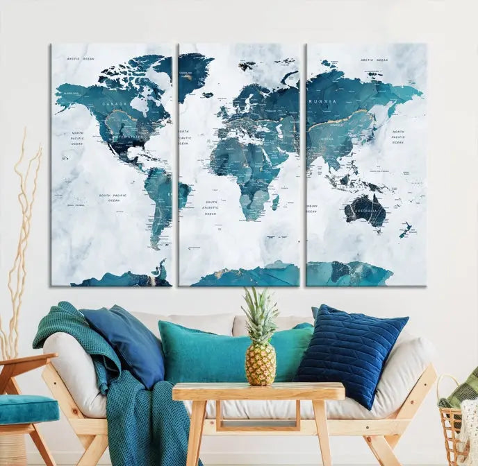 A Push Pin World Map with Antarctica, printed on museum-quality canvas portraying blue oceans, is displayed as a triptych above a dark wall.