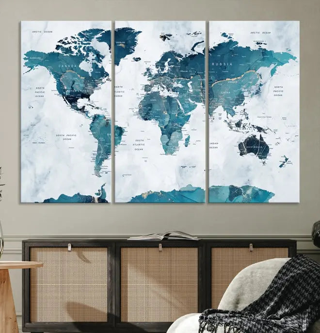 A Push Pin World Map with Antarctica, printed on museum-quality canvas portraying blue oceans, is displayed as a triptych above a dark wall.