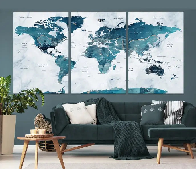 A Push Pin World Map with Antarctica, printed on museum-quality canvas portraying blue oceans, is displayed as a triptych above a dark wall.