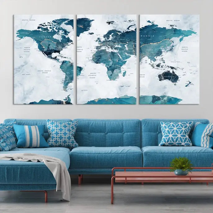 A Push Pin World Map with Antarctica, printed on museum-quality canvas portraying blue oceans, is displayed as a triptych above a dark wall.