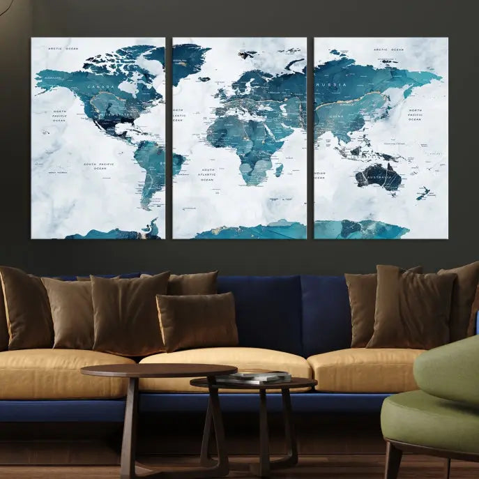 A Push Pin World Map with Antarctica, printed on museum-quality canvas portraying blue oceans, is displayed as a triptych above a dark wall.