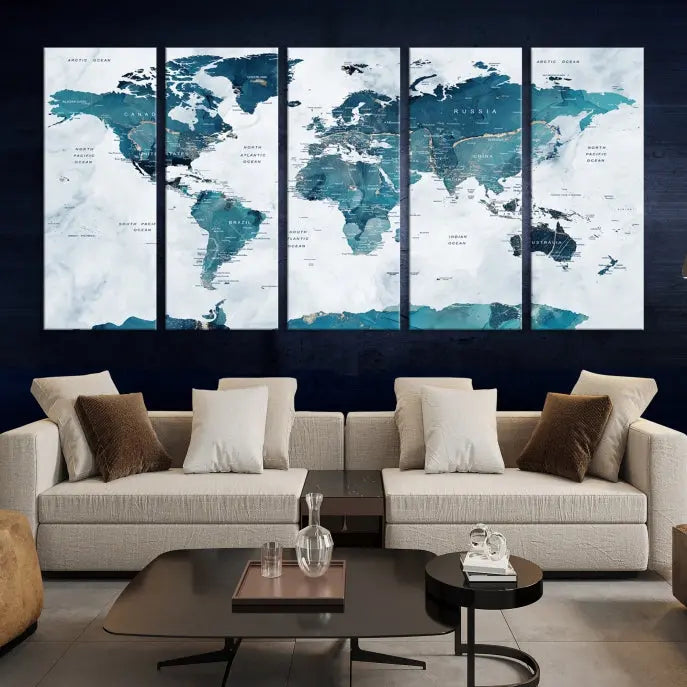 A Push Pin World Map with Antarctica, printed on museum-quality canvas portraying blue oceans, is displayed as a triptych above a dark wall.