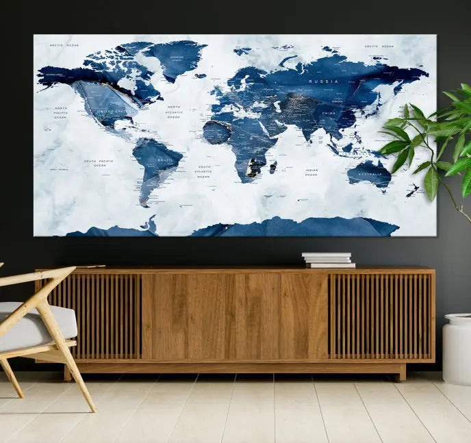 The Navy Blue World Map with Antarctica Wall Art Canvas Print, featuring a stunning blend of blue and white on a museum-quality canvas, elegantly adorns a dark wall. This ready-to-hang masterpiece enhances the room's sophisticated ambiance.