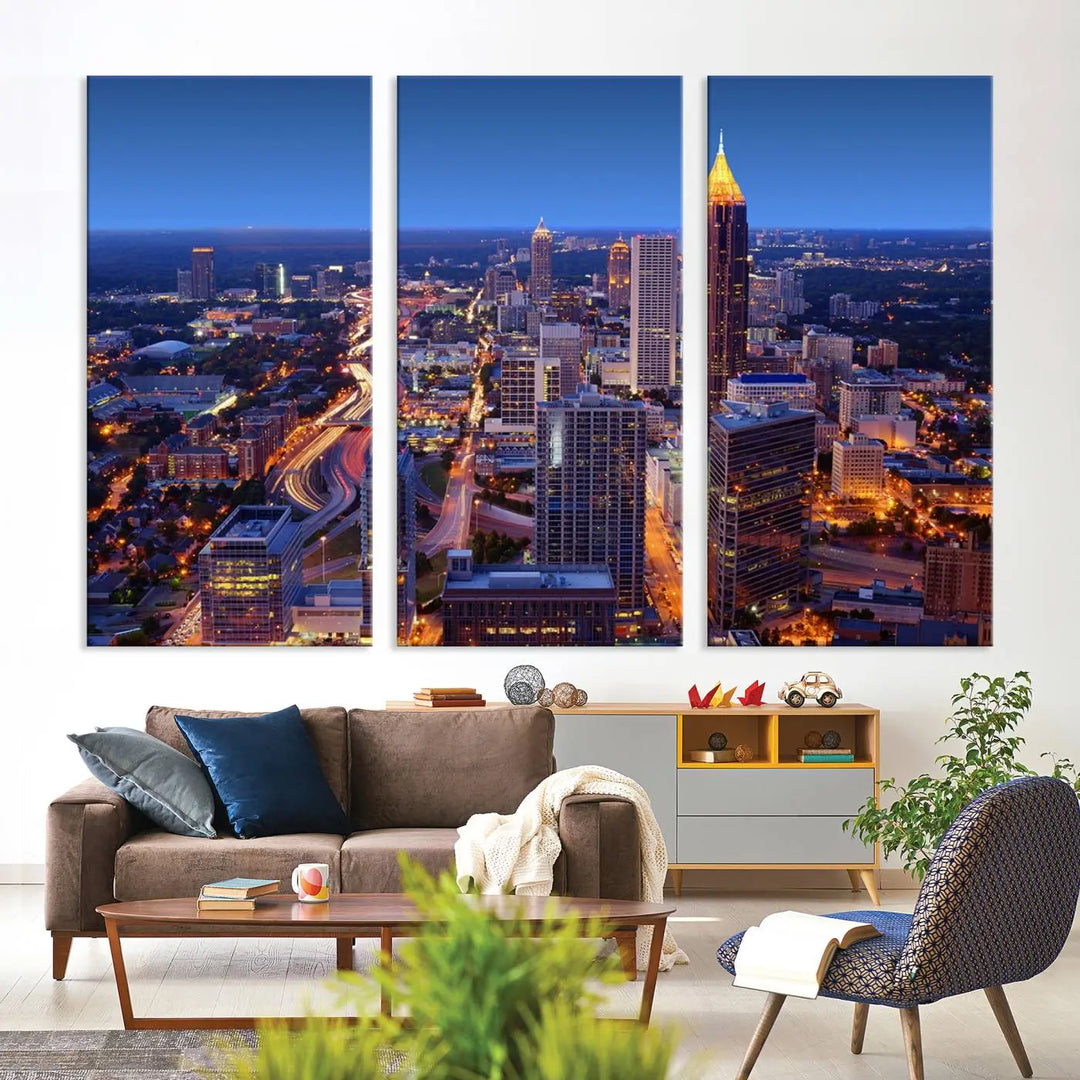 The triptych titled "Atlanta Wall Art Canvas Print" decorates the wall in a modern living room. This museum-quality artwork of a cityscape at night is ready to hang and features a UV-protective coating that ensures lasting vibrancy and elegance.