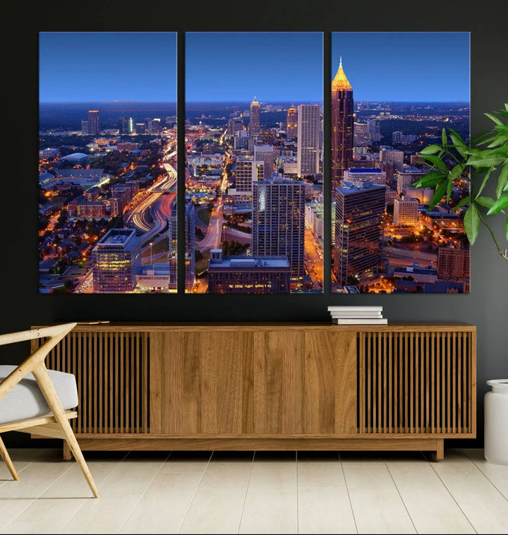 The triptych titled "Atlanta Wall Art Canvas Print" decorates the wall in a modern living room. This museum-quality artwork of a cityscape at night is ready to hang and features a UV-protective coating that ensures lasting vibrancy and elegance.