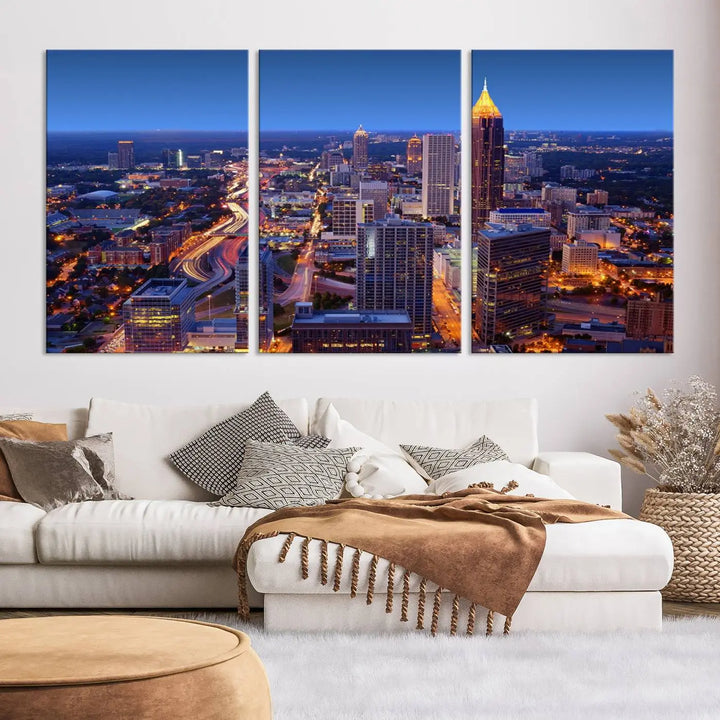 The triptych titled "Atlanta Wall Art Canvas Print" decorates the wall in a modern living room. This museum-quality artwork of a cityscape at night is ready to hang and features a UV-protective coating that ensures lasting vibrancy and elegance.