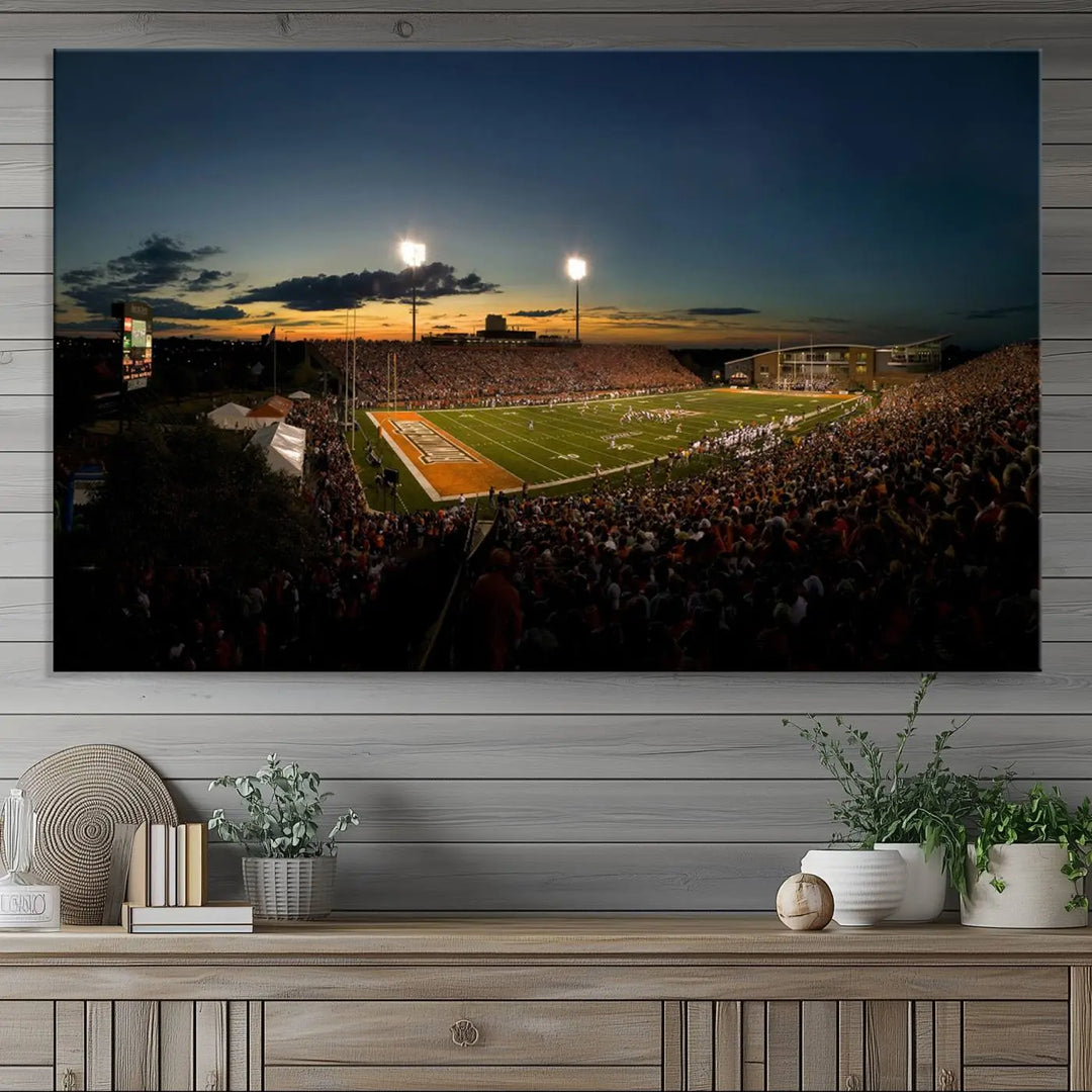 Experience the vibrant energy of game day with the Ball State Cardinals Football Team Print - Muncie Scheumann Stadium Wall Art Canvas Print. This stunning artwork captures a sunset-lit football stadium, alive with a match in progress and spectators filling the stands under floodlights, all rendered on museum-quality canvas.