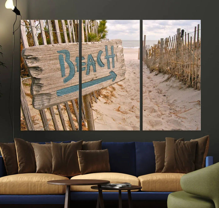 The Beach Is Calling You Wall Art Canvas Print features a sandy beach path with a wooden beach sign and arrow pointing to the ocean, beautifully displayed on museum-quality canvases.