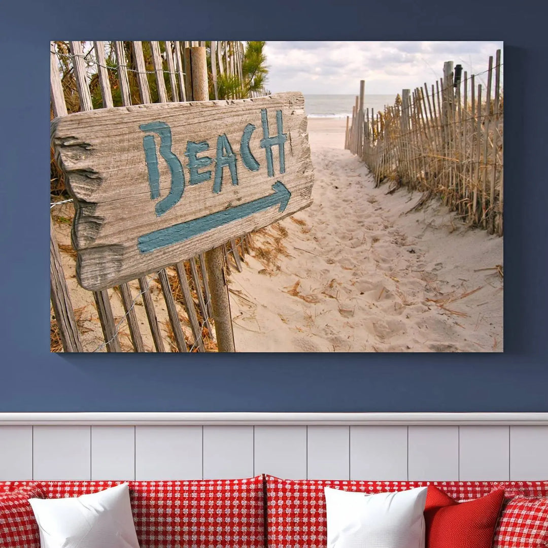 The Beach Is Calling You Wall Art Canvas Print features a sandy beach path with a wooden beach sign and arrow pointing to the ocean, beautifully displayed on museum-quality canvases.