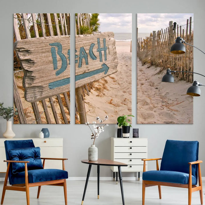 The Beach Is Calling You Wall Art Canvas Print features a sandy beach path with a wooden beach sign and arrow pointing to the ocean, beautifully displayed on museum-quality canvases.