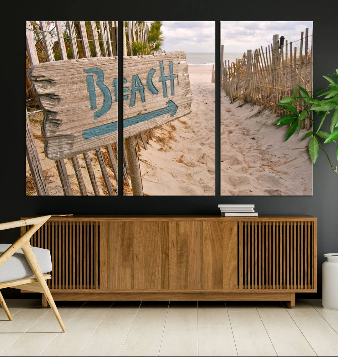 The Beach Is Calling You Wall Art Canvas Print features a sandy beach path with a wooden beach sign and arrow pointing to the ocean, beautifully displayed on museum-quality canvases.