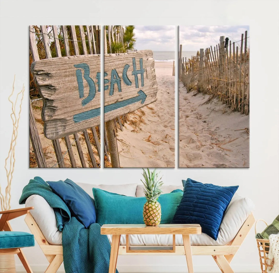 The Beach Is Calling You Wall Art Canvas Print features a sandy beach path with a wooden beach sign and arrow pointing to the ocean, beautifully displayed on museum-quality canvases.