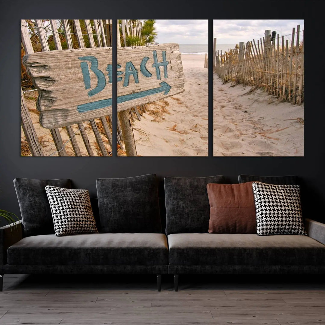 The Beach Is Calling You Wall Art Canvas Print features a sandy beach path with a wooden beach sign and arrow pointing to the ocean, beautifully displayed on museum-quality canvases.