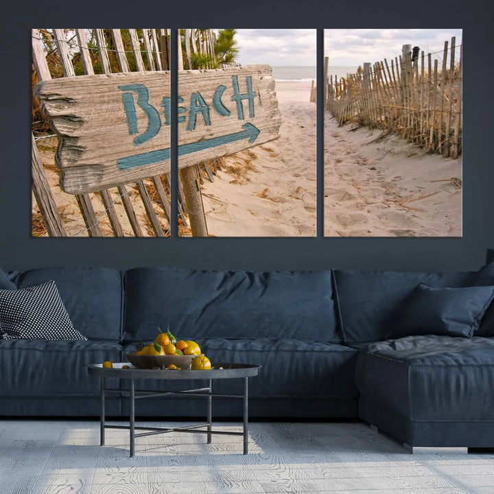 The Beach Is Calling You Wall Art Canvas Print features a sandy beach path with a wooden beach sign and arrow pointing to the ocean, beautifully displayed on museum-quality canvases.