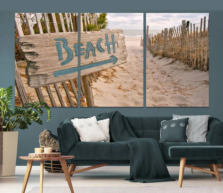 The Beach Is Calling You Wall Art Canvas Print features a sandy beach path with a wooden beach sign and arrow pointing to the ocean, beautifully displayed on museum-quality canvases.