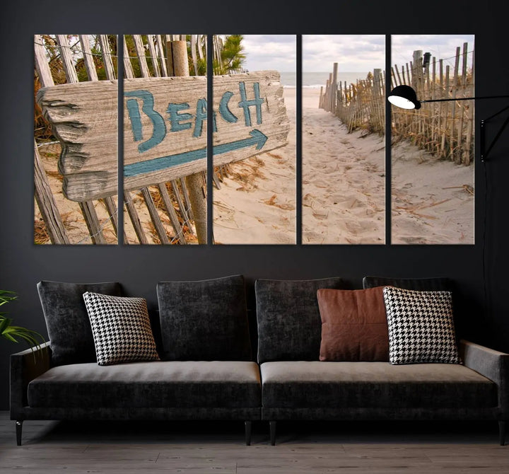 The Beach Is Calling You Wall Art Canvas Print features a sandy beach path with a wooden beach sign and arrow pointing to the ocean, beautifully displayed on museum-quality canvases.