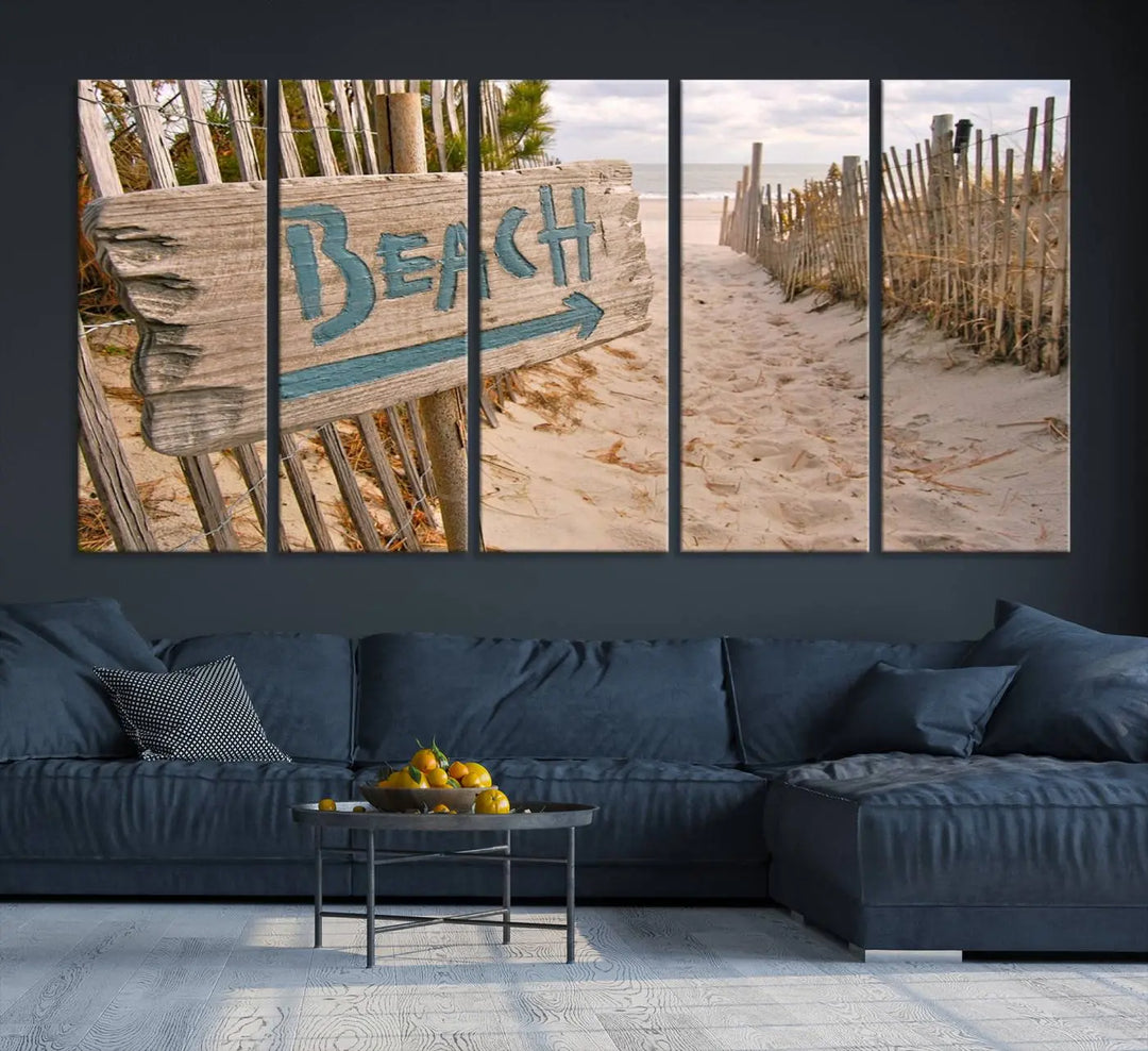 The Beach Is Calling You Wall Art Canvas Print features a sandy beach path with a wooden beach sign and arrow pointing to the ocean, beautifully displayed on museum-quality canvases.