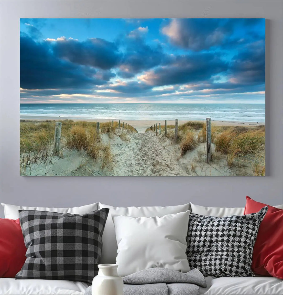 The "Beach Ocean Sun Sand Wall Art Canvas Print" is a triptych showcasing a beach path with grass leading to the ocean under a dramatic cloudy sky. This museum-quality canvas includes a UV-protective coating for longevity and vibrancy, and it comes ready to hang for effortless elegance.