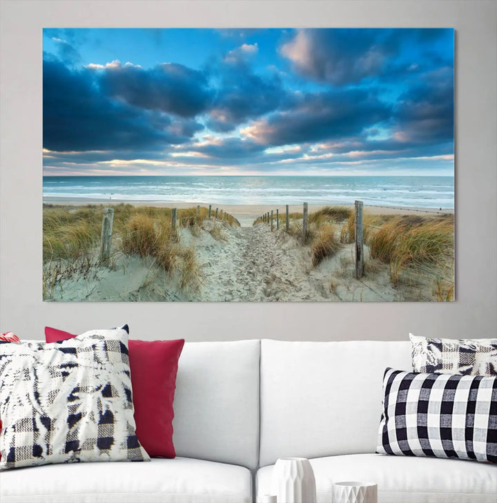 The "Beach Ocean Sun Sand Wall Art Canvas Print" is a triptych showcasing a beach path with grass leading to the ocean under a dramatic cloudy sky. This museum-quality canvas includes a UV-protective coating for longevity and vibrancy, and it comes ready to hang for effortless elegance.