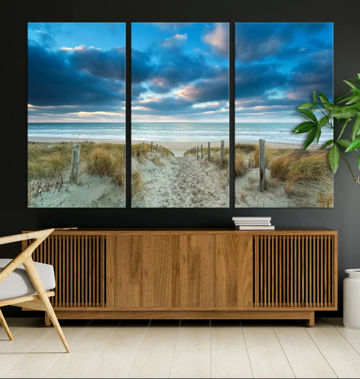 The "Beach Ocean Sun Sand Wall Art Canvas Print" is a triptych showcasing a beach path with grass leading to the ocean under a dramatic cloudy sky. This museum-quality canvas includes a UV-protective coating for longevity and vibrancy, and it comes ready to hang for effortless elegance.